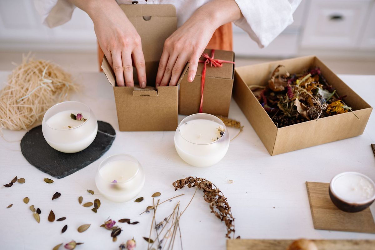 Hands assembling candles and components into kraft subscription boxes on a packing bench
